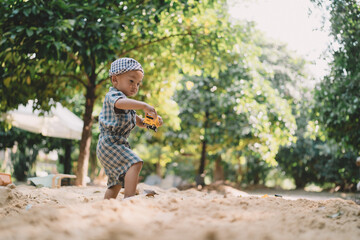 In the summer garden, a boy joins other children playing with toys in the sand, each person...