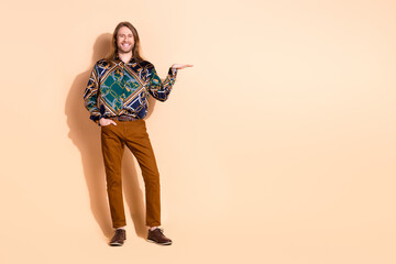 Young stylish man in colorful shirt and brown pants gesturing happily against beige background for fashion and lifestyle concept