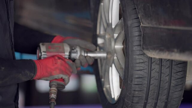 A person is working on a car, specifically changing a tire. The tire is located on the back of the car, and the person is using a tool to remove it