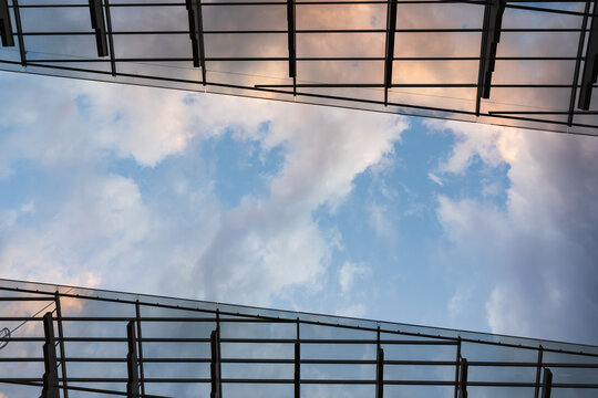 Modern architecture: a low-angle view of a glass ceiling or facade with a metal structure against a cloudy sky with sunset hues.