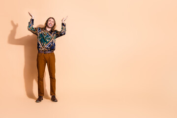 Charismatic young man in a stylish printed shirt making a joyful gesture on a soft beige background with studio lighting