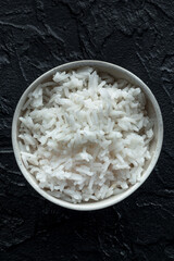 White rice, cooked. A bowl of boiled long grain rice, a simple side dish, top shot on a black background