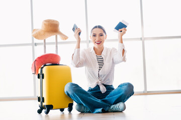 Young woman with yellow suitcase holding passport and phone, excited for her journey, seated at airport terminal