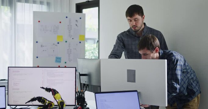 Team adult male engineer collaborate on robotic hand project using AI code solutions machine learning at tech workspace. Artificial intelligence interface, collaboration support prototype development.