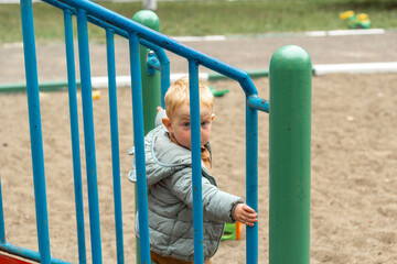 A little red-haired boy in a jacket walks down the steps from the slide. Outdoor walks