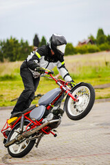 Man in a black biker suit and helmet performs extreme stunts on a motorcycle in mid-air. Dynamic...