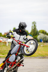 Man in a black biker suit and helmet performs extreme stunts on a motorcycle in mid-air. Dynamic...
