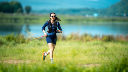 A woman is running in a field with a stick in her hand. The stick is red and blue