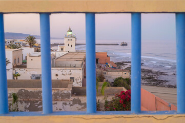 Sidi Ifni coastal landscape with lighthouse viewed through blue railing at sunset