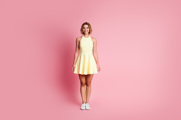 Lovely young woman in yellow dress smiling against pink background posing gracefully with elegance...