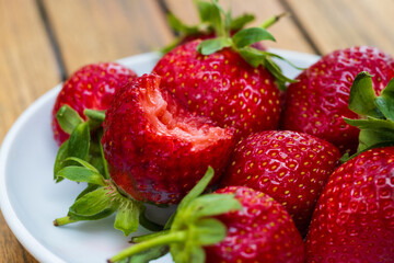 Close-up of ripe red strawberries in a white plate. Huge red strawberries with green leaves. Strawberries are bitten, teeth marks on the berry. Selective focus