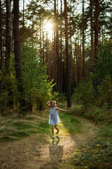 Fototapeta premium Young girl joyfully running along a forest path, surrounded by tall trees and vibrant greenery, capturing the essence of childhood freedom and nature exploration