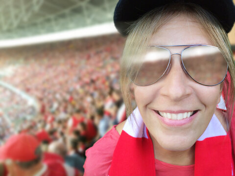 Portrait of a Smiling woman wearing sunglasses and team colours in the stands at a sports event