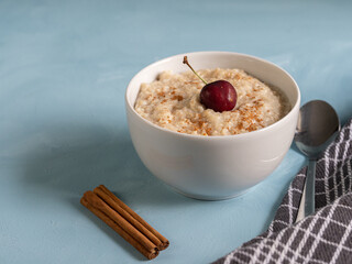 Porridge bowl with fresh fruit and cinnamon on light blue background. Healthy, vegetarian breakfast ready to take care of yourself in the morning