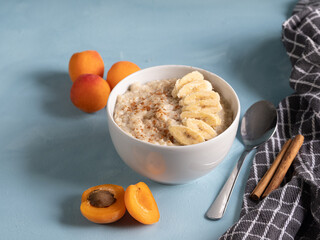 Bowl of porridge with cinnamon and banana accompanied by fresh fruit and on a blue background. Healthy, vegetarian and energized breakfast
