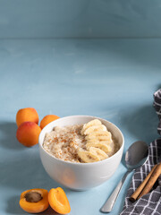 Bowl of porridge with cinnamon and banana accompanied by fresh fruit and on a blue background. Healthy, vegetarian and energized breakfast