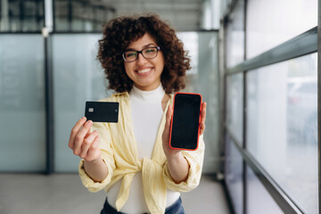 Shopping time, with credit card. Beautiful woman is standing indoors against blurred wall
