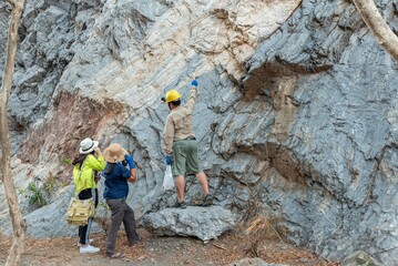 A geologist leading a group of people and showing them something in the rock face.