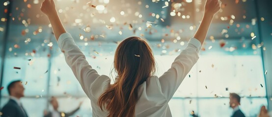 Back view of excited young woman celebrating with colleagues in modern office, confetti flying, coworkers cheering after successful project, wide-angle, blurred background.