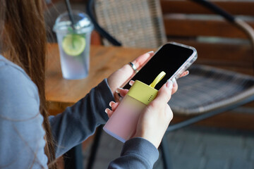 Close-up of a young woman plugging a yellow power bank into her smartphone. Modern lifestyle,...