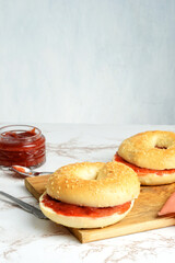 closeup sesame seed bagel with strawberry rhubarb jam on wood cutting board