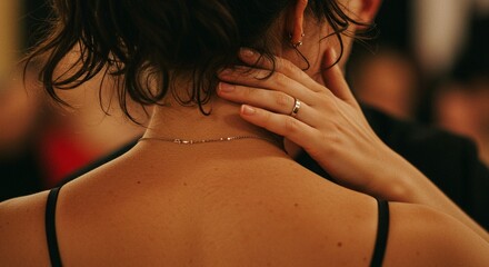 Close-up of a woman's back with a gold necklace and a hand resting on her neck with a wedding ring