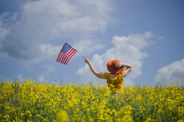 Woman with orange hat holding the American flag outdoors on a rapeseed yellow meadow.  4th of July...