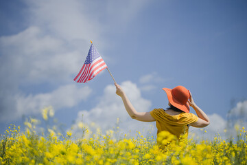 Woman with orange hat holding the American flag outdoors on a rapeseed yellow meadow.  4th of July...