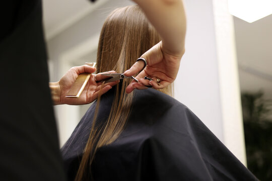 Unrecognisable hairdresser cutting female client hair with professional barber scissors and comb and making stylish haircut short bob hairstyle in beauty salon. Hair care, hair salon and hairstyling