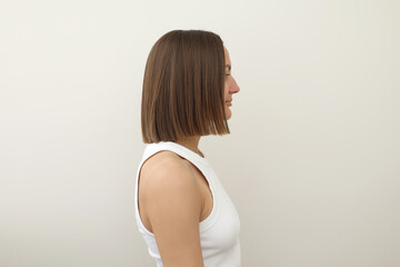 Side view of young woman with natural straight shoulder length brown hair on light background, emphasizing the hair texture and clean. Haircare, fashion, wellness, beauty, and lifestyle-related