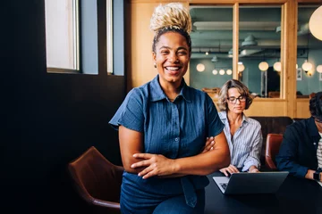 Selbstklebende Fototapeten Smiling woman standing confidently with colleagues working in the background © (JLco) Julia Amaral