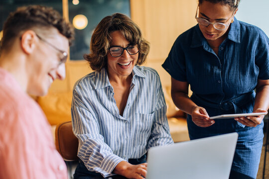 Three colleagues discussing work using a laptop and tablet in a modern office
