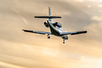 Private business jet flying under an orange sunset sky