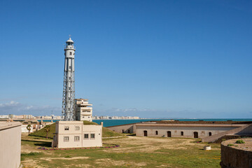 Metal lighthouse and historic coastal fortress in Cádiz under clear blue skies
