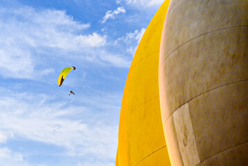 Paragliding in a blue sky with clouds and a yellow hot air balloon in the background.