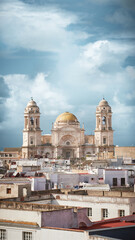 A vertical composition highlighting the impressive architecture of the Cádiz Cathedral and the traditional Andalusian rooftops surrounding it.