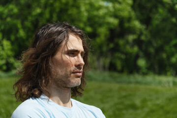 Portrait of thoughtful handsome caucasian brunette man with long curly hair enjoying nature and...
