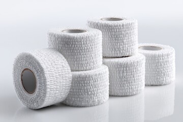 A close-up of multiple white medical elastic bandages rolled up and stacked on a white glossy surface, creating a visually appealing and clean composition for medical uses.