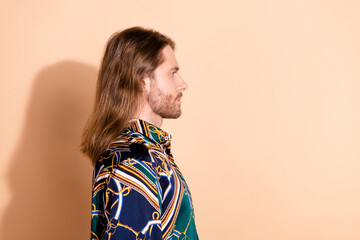 Profile view of a stylish young man with long hair and a vibrant printed shirt against a beige...