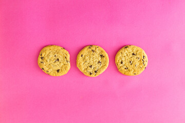 Three chocolate chip cookies on a pink background