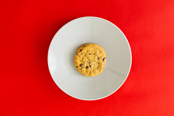 A cookie sits on a white plate on a red background