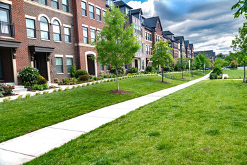 sidewalk along rows of modern brick townhouses with landscaping and a large lawn.