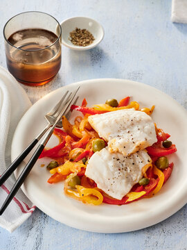 Delicious Cod Fillets Served With Colorful Bell Peppers and Garlic in a Cozy Dining Setting