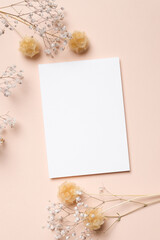 Blank wedding invitation or greeting card mockup on beige background with dried baby breath flowers, top view with copy space