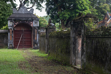 Open stone arch against the background of abandoned ancient buildings and antique ruins. In the background, broken door leaves. A mystical setting