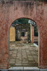 Open stone arch against the background of abandoned ancient buildings and antique ruins. In the background, broken door leaves. A mystical setting