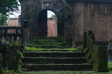 Open stone arch against the background of abandoned ancient buildings and antique ruins. In the background, broken door leaves. A mystical setting