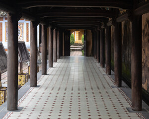 Outdoor long passage with round wooden columns on the sides. An open archway in the distance. 