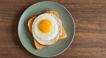 Fried egg on toast served on green plate against wooden background