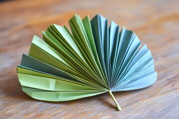 Folded origami paper creating a decorative palm leaf with green and blue hues, resting on a wooden surface